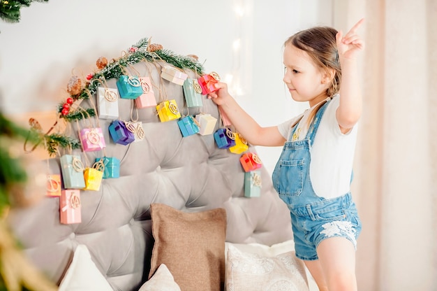 Foto kleines mädchen, das zu hause handgemachten adventskalender mit geschenkbox hält. diy adventskalender für kinder