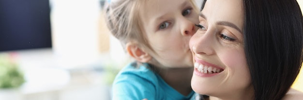 Kleines Mädchen, das zu Hause lächelnde Mutter küsst