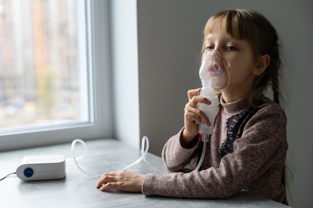 Kleines Mädchen, das zu Hause mit Zerstäuber inhaliert. Kinder Asthma Inhalator Inhalationsvernebler Dampf krank Husten Konzept Horizontal