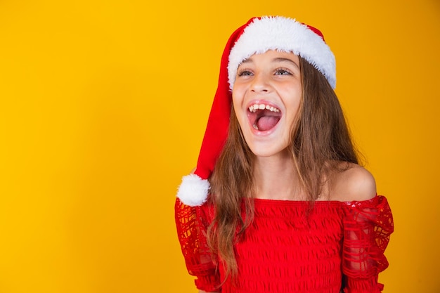 Kleines Mädchen, das zu Weihnachten gekleidet ist, verzaubert mit offenem Mund auf gelbem Hintergrund.