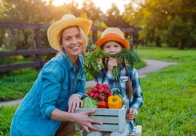 Kleines Mädchen der Kinder, das Mutter einen Korb des frischen organischen Gemüses mit dem Hausgarten hält.