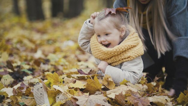 Kleines Mädchen der Mutter und ihrer Tochter, das in einem Herbstpark spielt - die Blätter werfen, Babylachen, Nahaufnahme