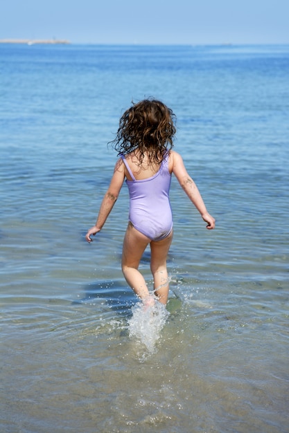 Kleines Mädchen des Brunette, das in Strandwasser läuft