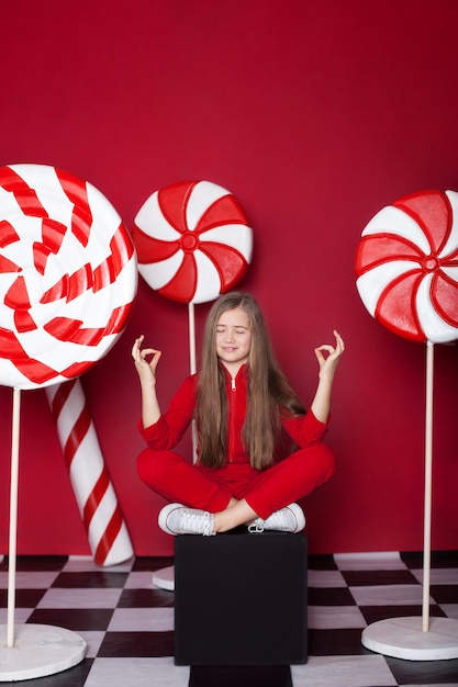 Kleines Mädchen entspannen mit riesigen Weihnachtsbonbons auf einem roten Hintergrund.