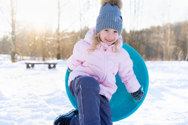 Kleines Mädchen fährt die Rutsche auf dem Eis herunter fröhliche Kindergefühle vom Winterspaß