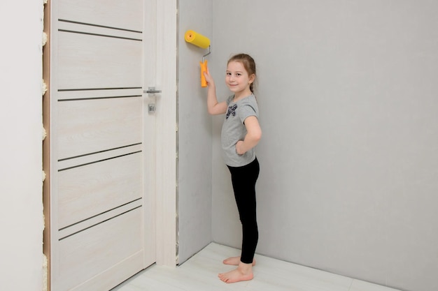 Kleines Mädchen fährt mit einem Farbroller in einem renovierten Haus an der Wand entlang