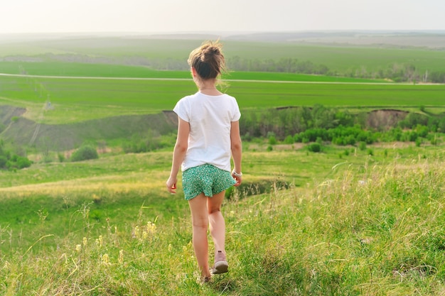 Kleines Mädchen geht auf einer grünen Wiese mit Blick auf die hügelige Landschaft