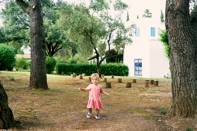Kleines Mädchen geht auf einer Lichtung in der Nähe von Baumstümpfen im Hof eines Hauses