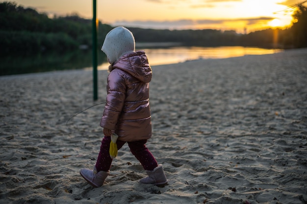 Kleines Mädchen geht bei Sonnenuntergang am Herbststrand spazieren