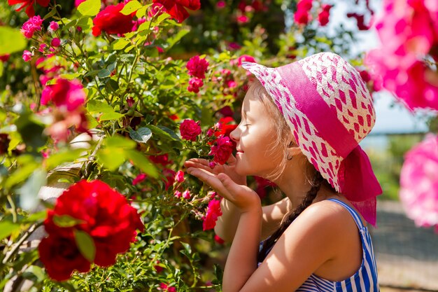 Kleines Mädchen geht im Garten mit blühenden Rosen. steht zurück in einem Hut mit einem rosa Band, Platz für Text