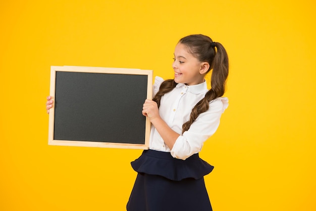 Kleines Mädchen großer Traum Kleines Kind mit Tafel für Schulwerbung auf gelbem Hintergrund Kleines Kind mit leeren Tafel für Ihren Text Kleines Schulmädchen, das Tafelkopienraum hält