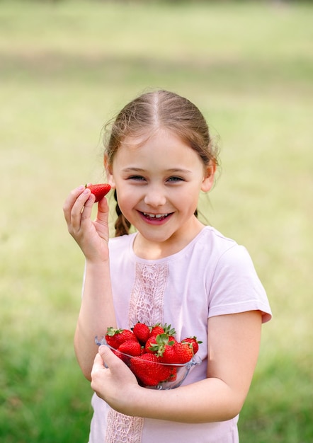 Kleines Mädchen Halteteller mit Erdbeeren in der Natur Garten- und Landwirtschaftskonzept Veganer Vegetarier Vertikal