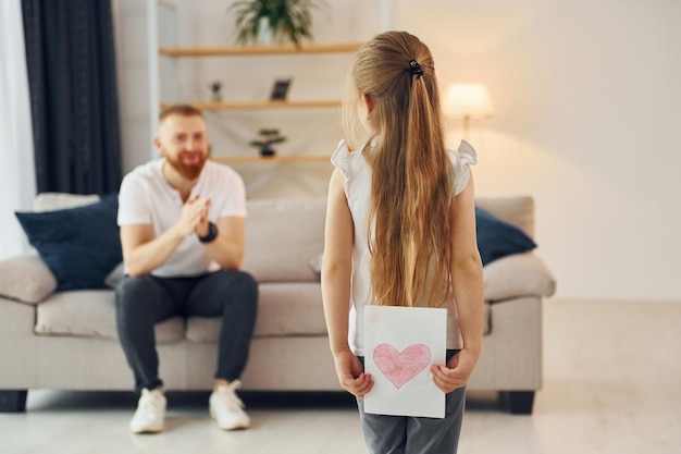 Kleines Mädchen hat Geschenk für Mann Vater mit seiner kleinen Tochter ist zusammen zu Hause