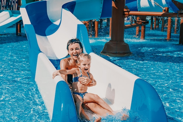 Kleines Mädchen im Badeanzug geht die blauen Rutschen hinunter zum Pool Mutter und Tochter spielen und schwimmen im Außenpool