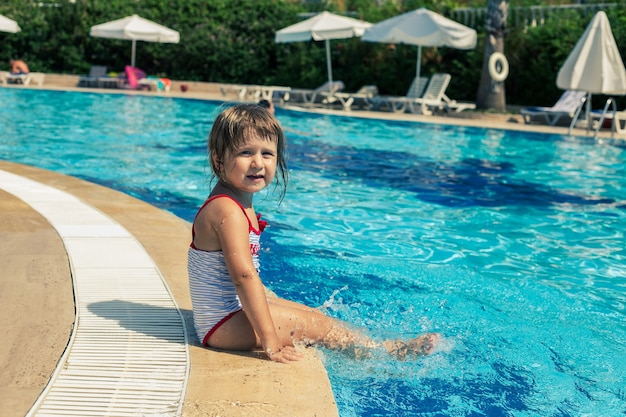 Kleines Mädchen im Badeanzug sitzt am Pool