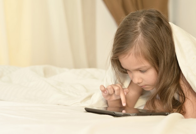 Kleines Mädchen im Bett mit Tablet-PC im Bett