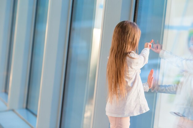 Kleines Mädchen im Flughafen nahe großem Fenster, während Sie auf das Verschalen warten