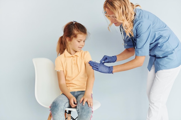 Kleines Mädchen im gelben Hemd Arzt in Uniform, der dem Patienten die Impfung vornimmt