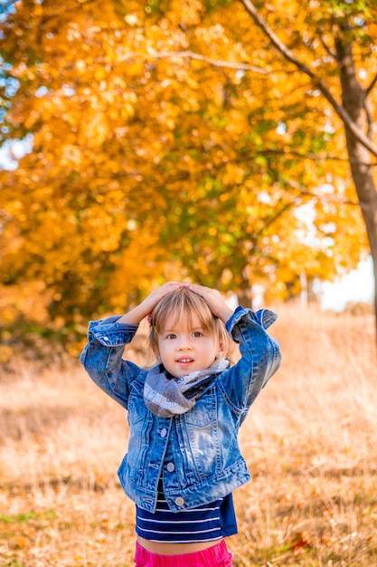 Kleines Mädchen im goldenen Park des Herbstes. Händchen haltend auf dem Kopf