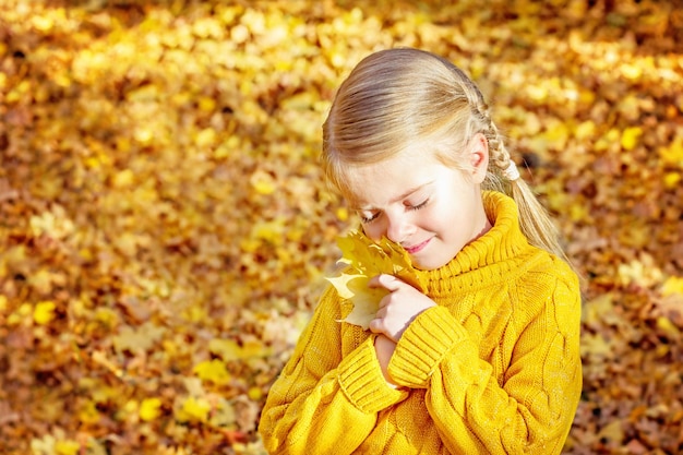 Foto kleines mädchen im herbstwald mit gelben ahornblättern in ihren händen.