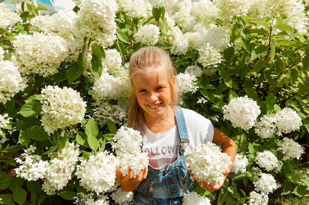 Kleines Mädchen im Hortensienpark. Fröhliches Kind. Kind schnuppert Hortensie im Garten.