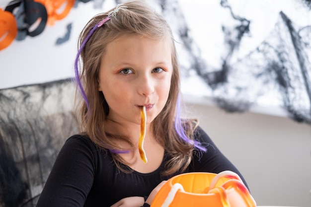 kleines Mädchen im Kostüm der Hexe, die Kürbisbuchse mit Süßigkeiten hält und Halloween zu Hause feiert