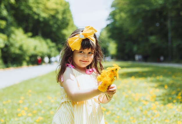 Kleines Mädchen im Park, das an einem sonnigen Sommertag gelbe Löwenzahnblumen pflückt