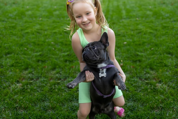 Kleines Mädchen im Park, das versucht, eine französische Bulldogge aufzuheben