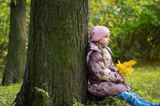 Kleines Mädchen im Park vor dem Hintergrund von Laub und Bäumen