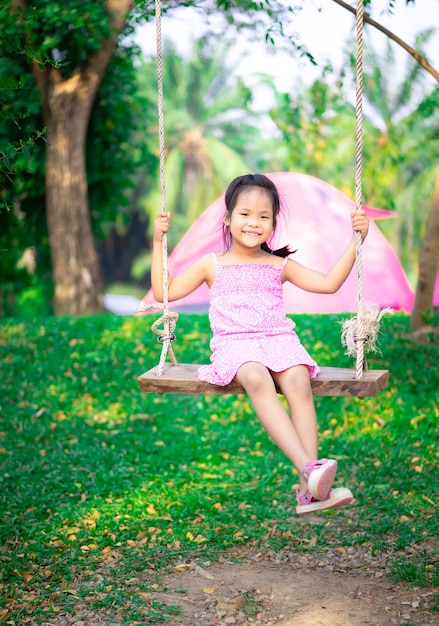 Kleines Mädchen im rosa Kleid, das auf einer Schaukel beim Zelten sitzt