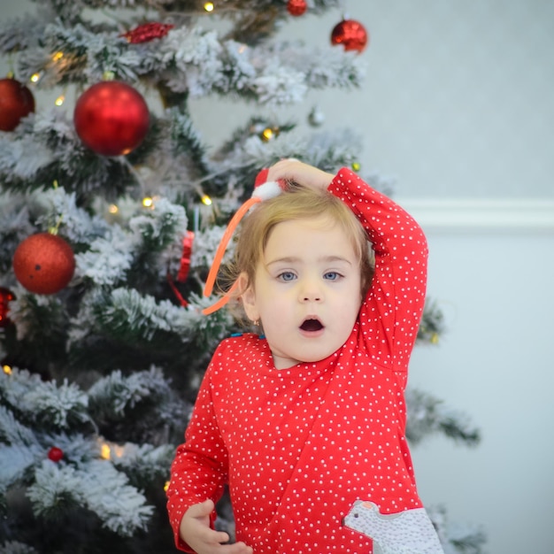 Kleines Mädchen im roten Kleid, das im Raum mit Weihnachtsdekorationen spielt