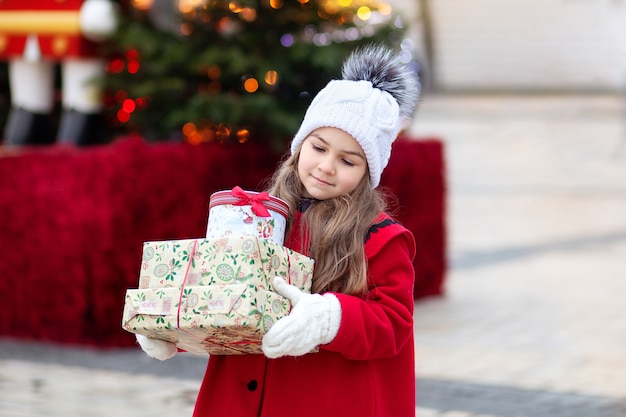 Kleines Mädchen im roten Mantel mit Weihnachtsgeschenken