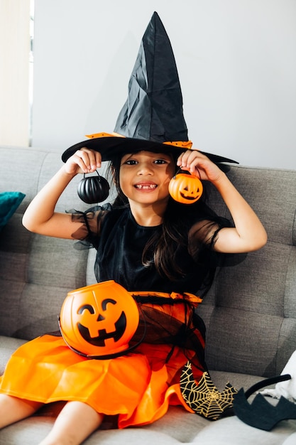 Kleines Mädchen im schwarzen Hexenkostüm mit Kürbissen für Halloween