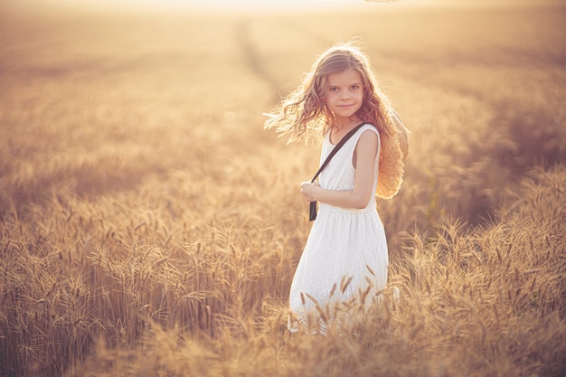 kleines Mädchen im weißen Kleid und im Strohhut am abendlichen Weizenfeld