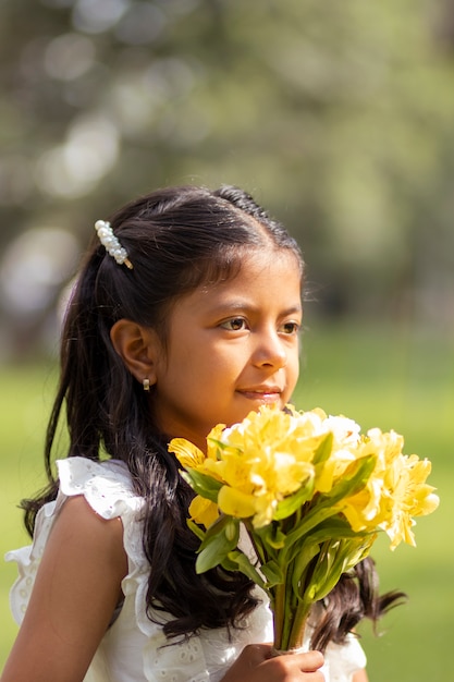 Kleines Mädchen im weißen Kleid und mit einem niedlichen Blumenstrauß in der Hand