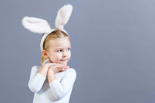 Kleines Mädchen im weißen Osterhasen-Kostüm auf einer grauen Wand. Schönes Baby, das in Richtung Kopierraum schaut.