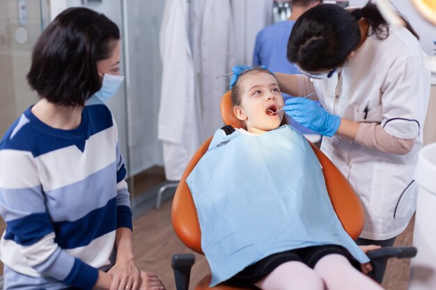 Kleines Mädchen im Zuge der Zahnbehandlung vom jungen Zahnarzt im Büro. Zahnmediziner während der Kinderhöhlenberatung in der Stomatologie-Büro mit moderner Technologie.