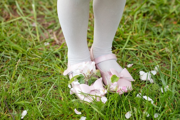 Kleines Mädchen in den rosa Schuhen auf grünem Gras im blühenden Park. Nahaufnahme Füße.