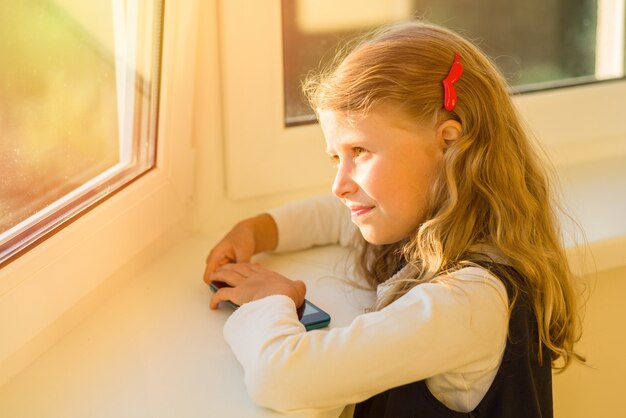 Kleines Mädchen in der Schuluniform, die heraus das Fenster schaut