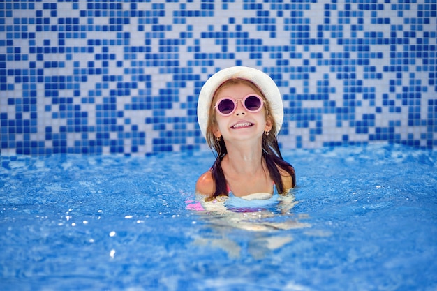 Kleines Mädchen in der Sonnenbrille und im Hut mit Einhorn Swimmingpool im im Freien des Luxusresorts auf Sommerferien auf tropischer Strandinsel