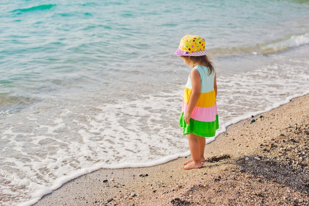 Kleines Mädchen in einem Badeanzug, der ihre Beine im Meer spritzt