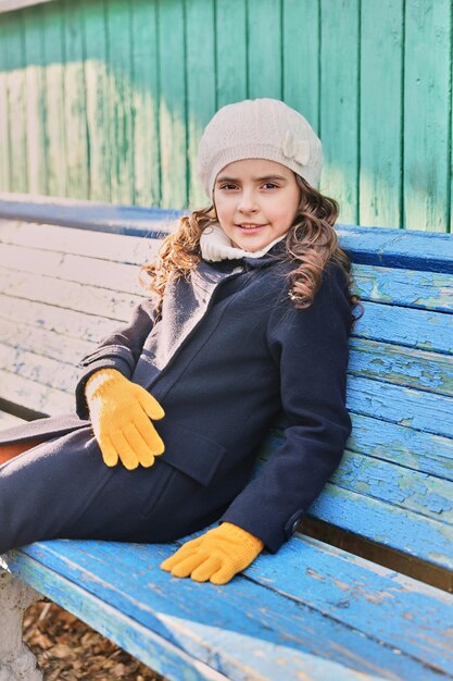 Kleines Mädchen in einem blauen Mantel auf einer Parkbank im Herbst. Foto in hoher Qualität