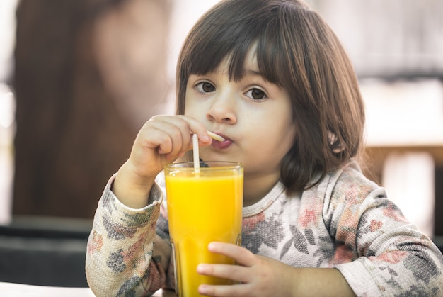 Kleines Mädchen in einem Café, das Saft trinkt