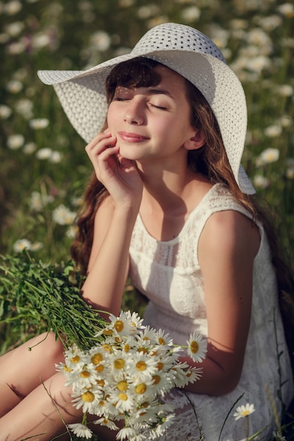 Kleines Mädchen in einem Feld von Gänseblümchen. Teenie-Mädchen in Hut und Kleid genießt den Frühling im Gänseblümchen-Feld. Das Konzept und die Idee einer glücklichen Kindheit