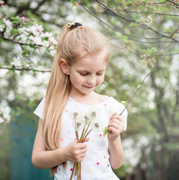 Kleines Mädchen in einem Frühlingsgarten mit weißem Löwenzahn in den Händen