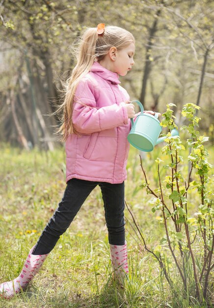 Kleines Mädchen in einem Garten mit grüner Gießkanne