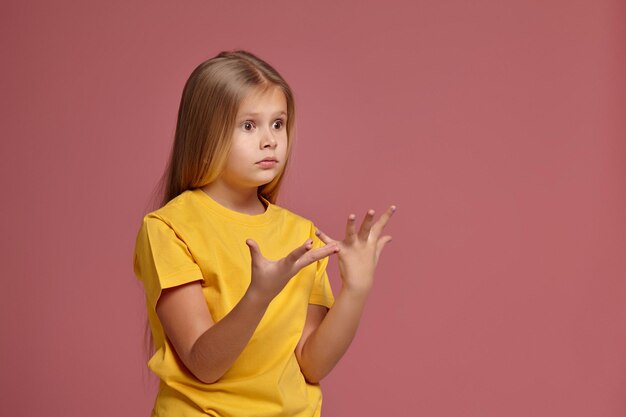 Kleines Mädchen in einem gelben T-Shirt. überrascht zeigt hände