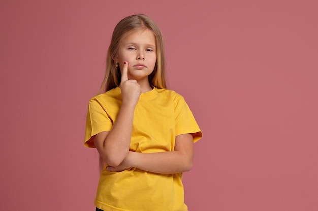 Kleines Mädchen in einem gelben T-Shirt zeigt nachdenklich Finger