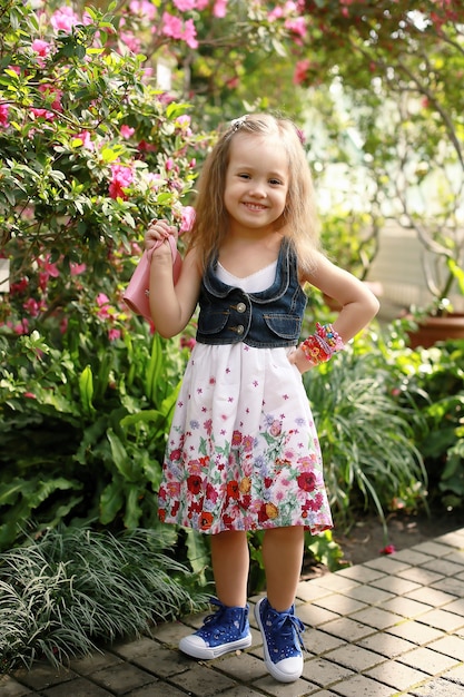 kleines Mädchen in einem Kleid mit Blumen im Botanischen Garten.