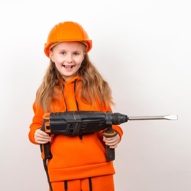 Kleines Mädchen in einem orangefarbenen Anzug und einem Bauhelm, der ein Puncher-Konzept eines jungen Arbeiters hält Portrait Child Builder weißer Hintergrund Tag der Arbeit